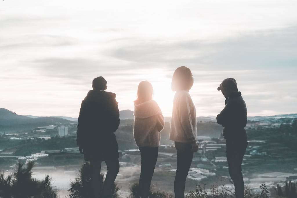 A group of friends standing on a hill, silhouetted against the sunset sky, enjoying a beautiful landscape view.